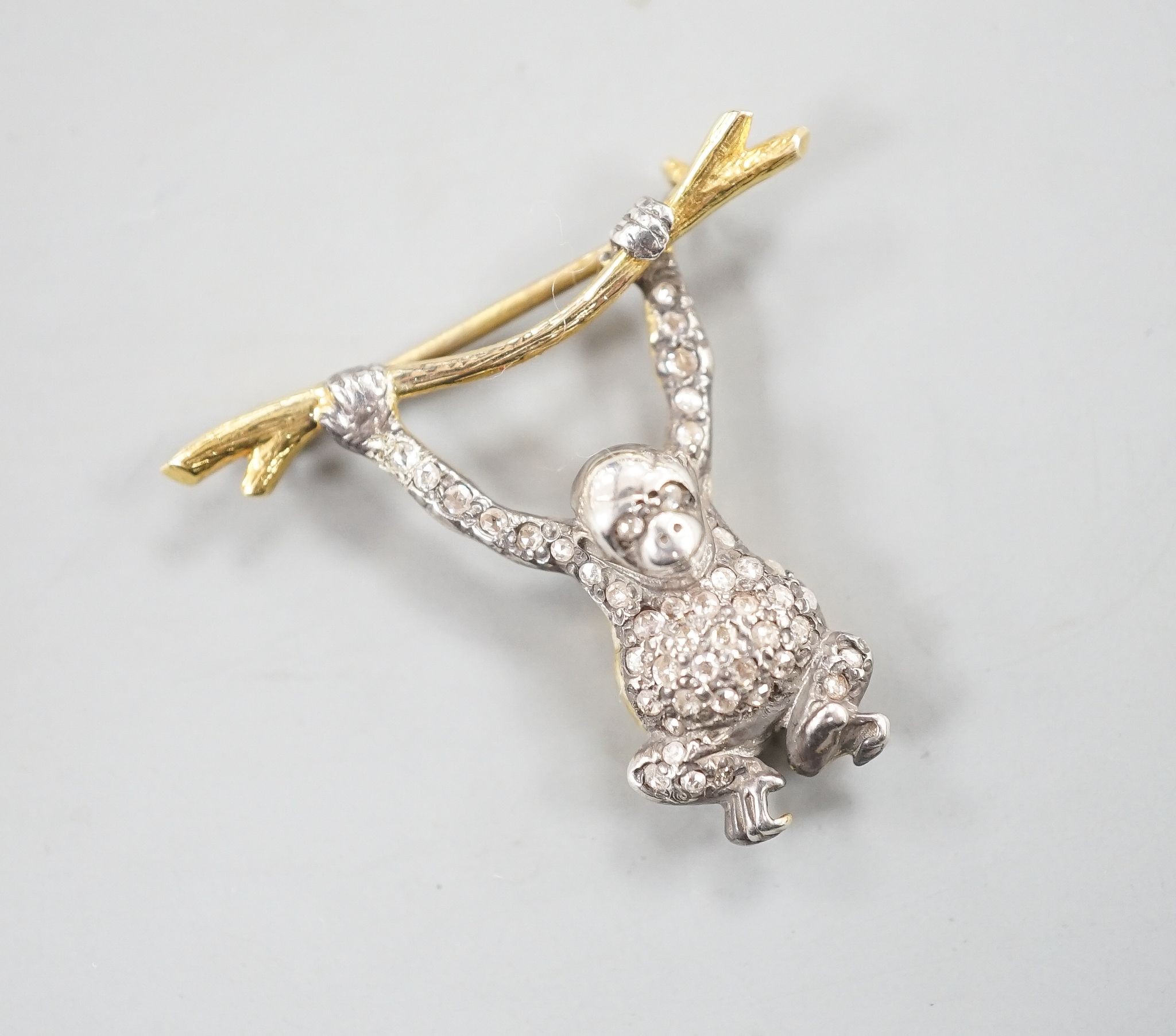 A Victorian style novelty white and yellow metal, diamond chip set brooch, modelled as a monkey hanging from a branch, 26mm drop, width 30mm.